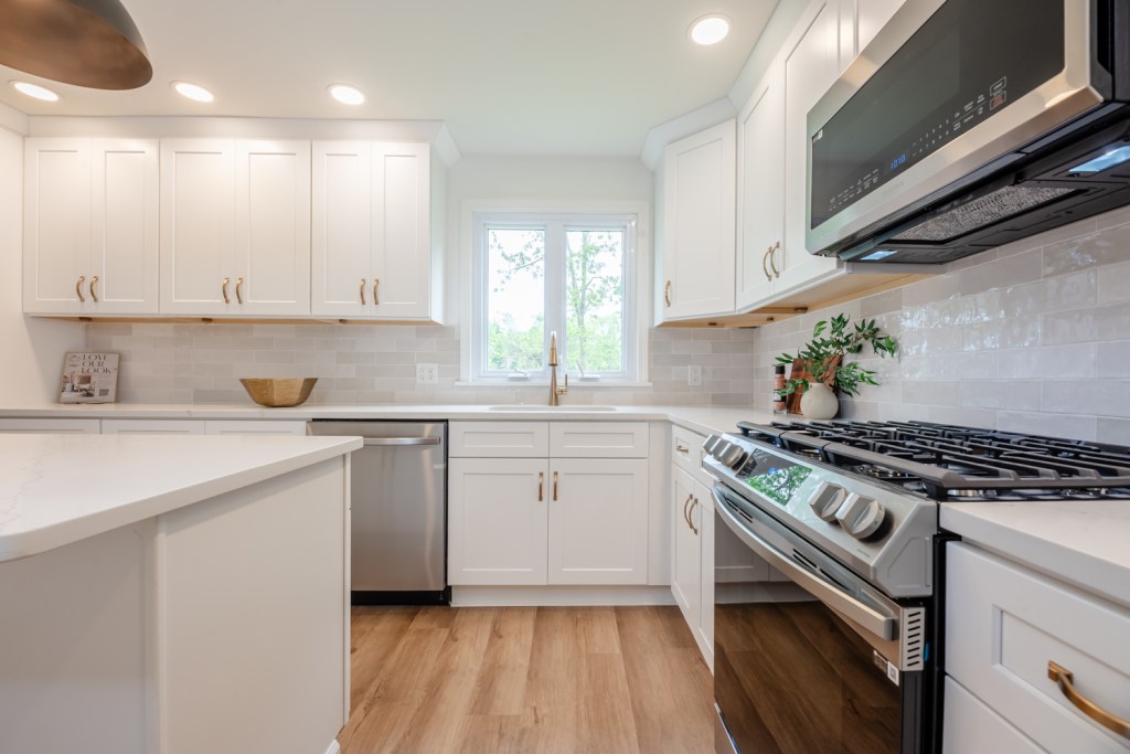 Modern kitchen with white cabinetry, stainless steel appliances, and a gas stove, featuring natural light from a window and decorative plants on the countertop. Updated Cape Cod Home in Penfield